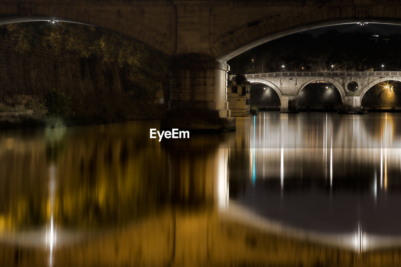 ILLUMINATED BRIDGE OVER RIVER AT NIGHT