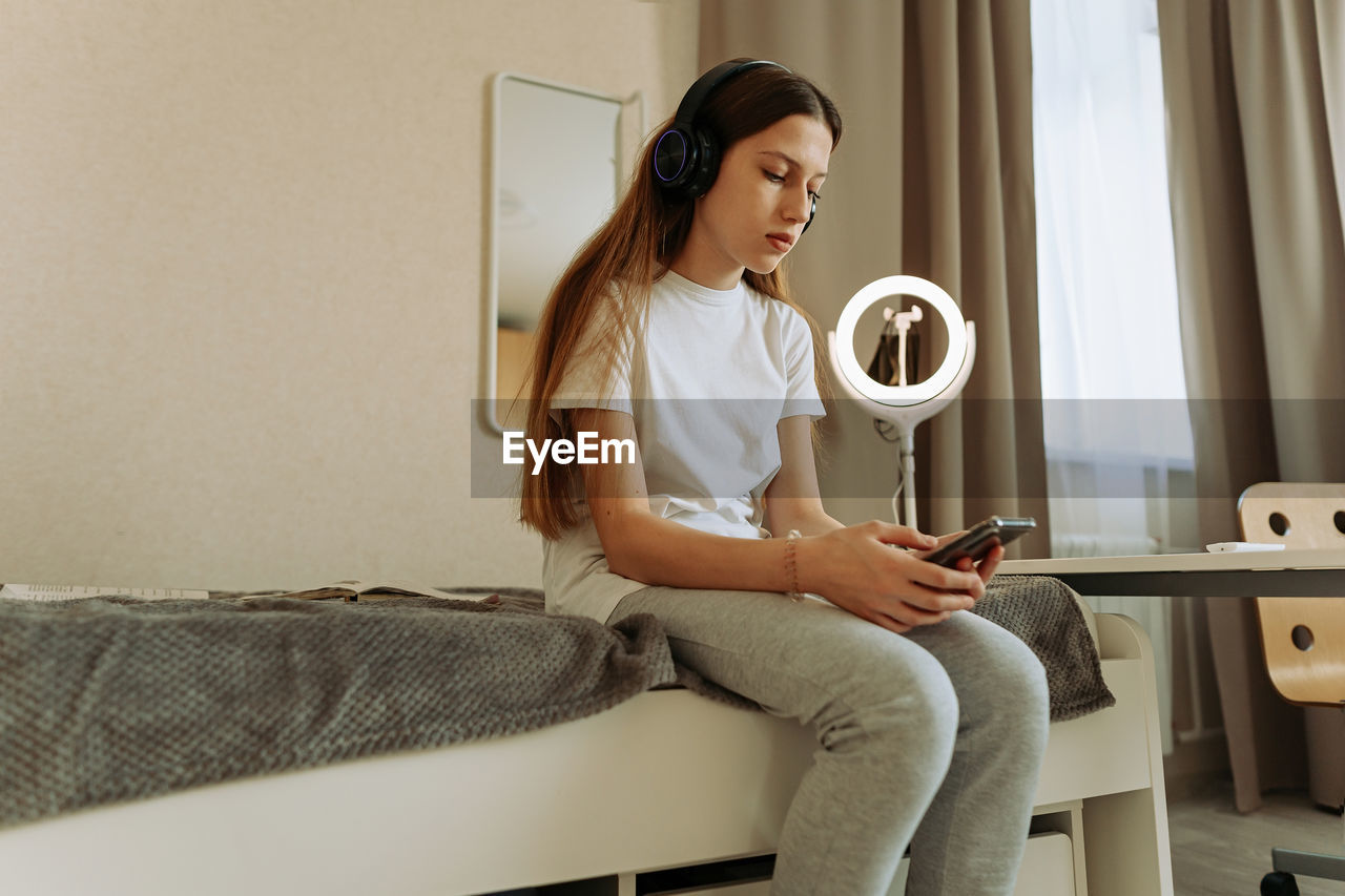 Generation z girl in headphones with a smartphone sits on the bed