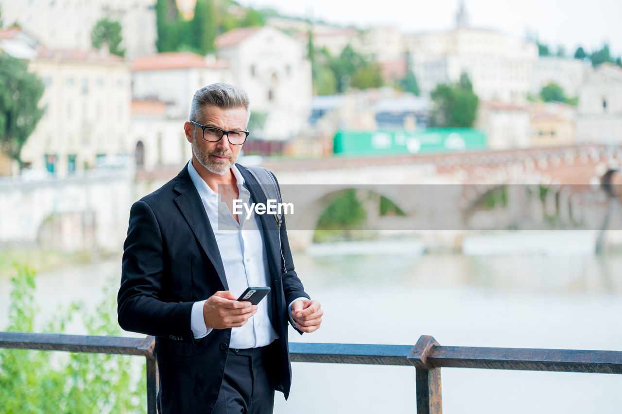 Businessman holding mobile phone while standing outdoors