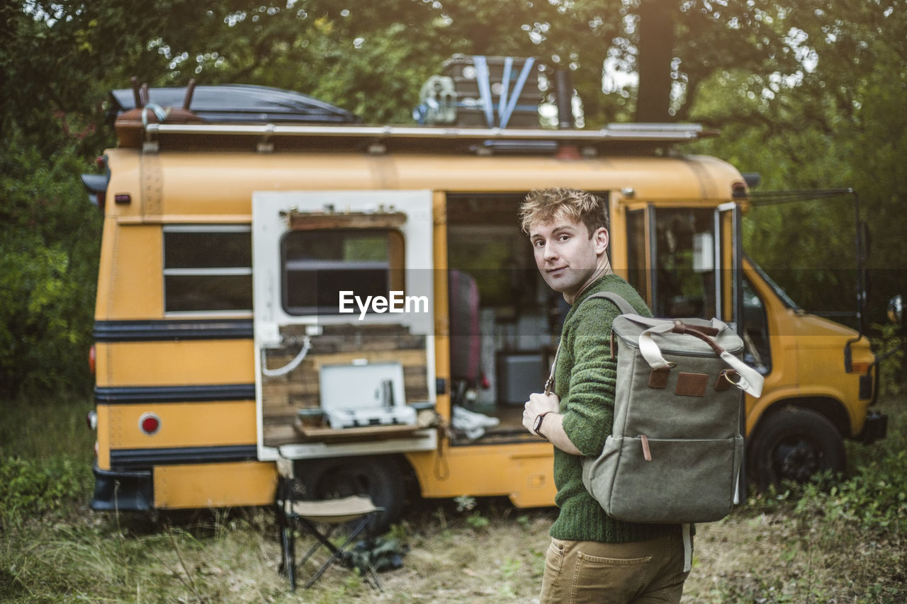 Rear view portrait of man with backpack walking towards motor home in forest during camping