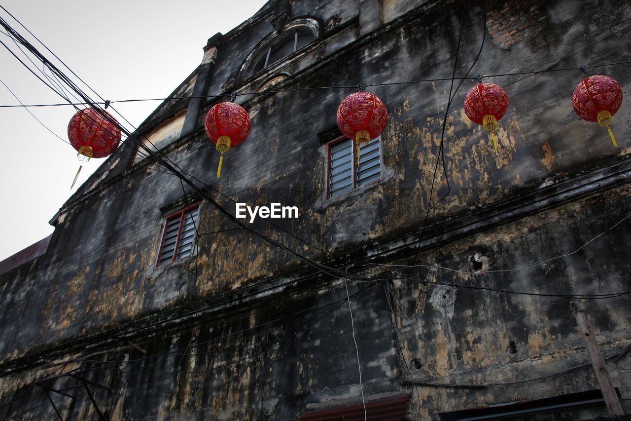 Low angle view of red lanterns hanging against abandoned building
