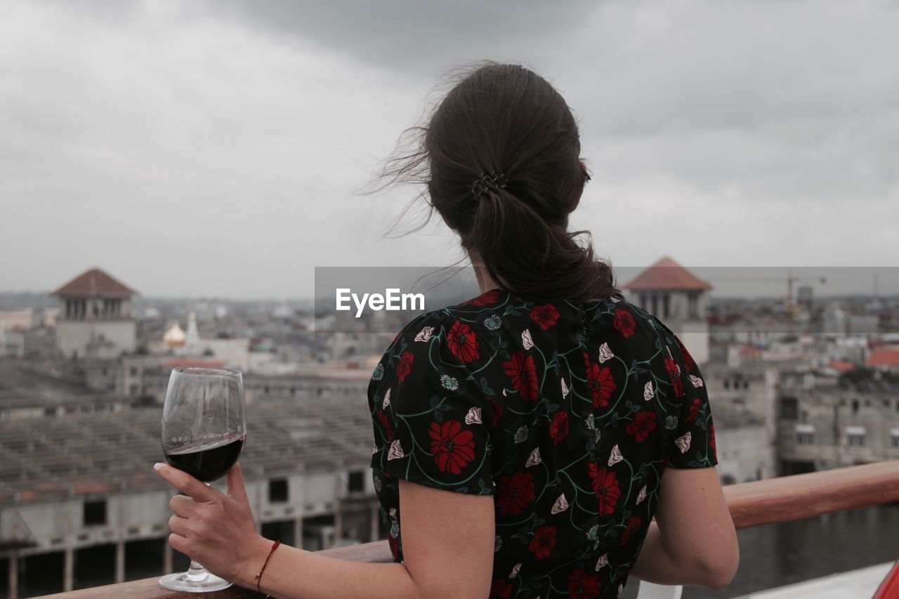 Rear view of woman holding wine glass against cityscape