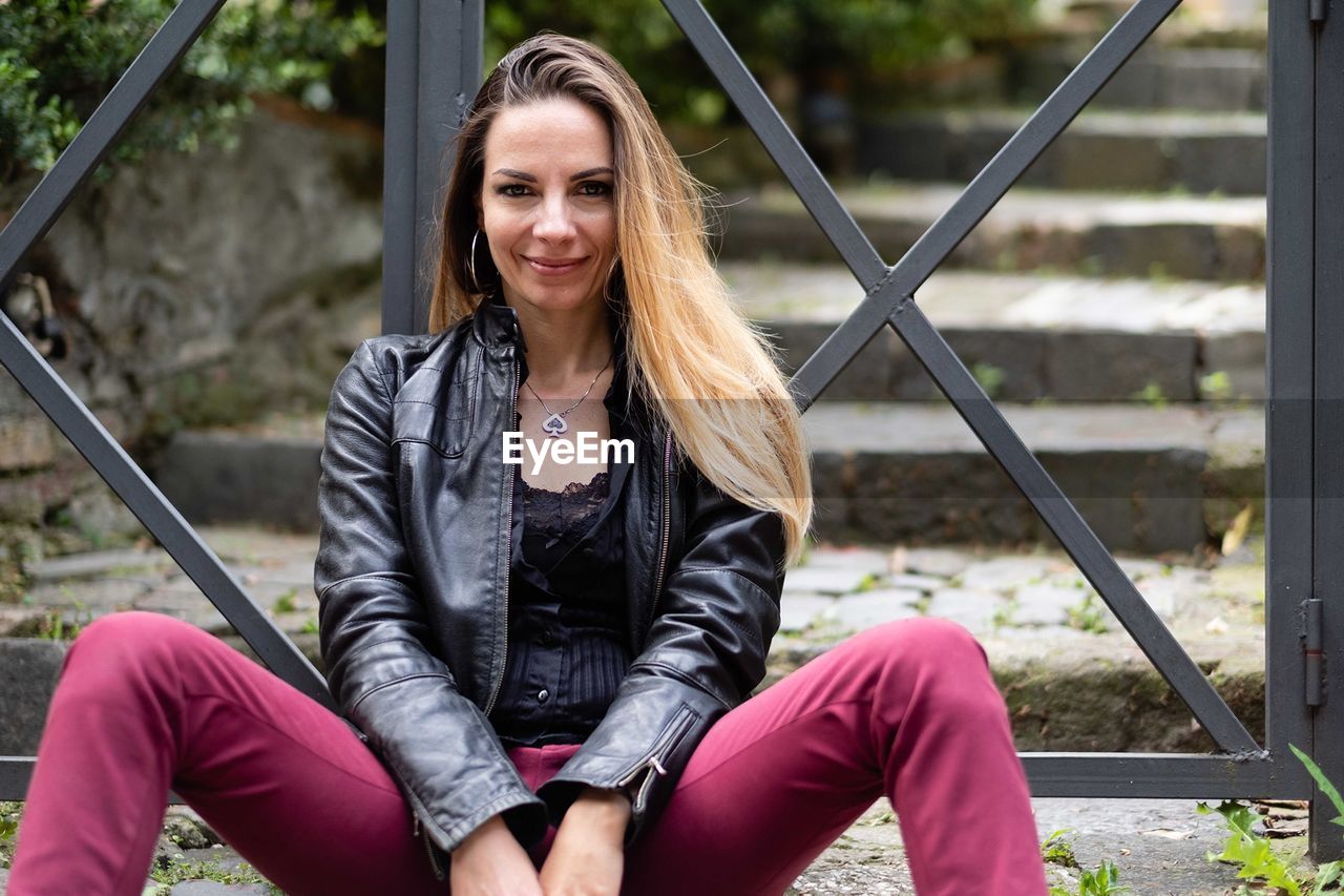 Portrait of smiling woman sitting against gate