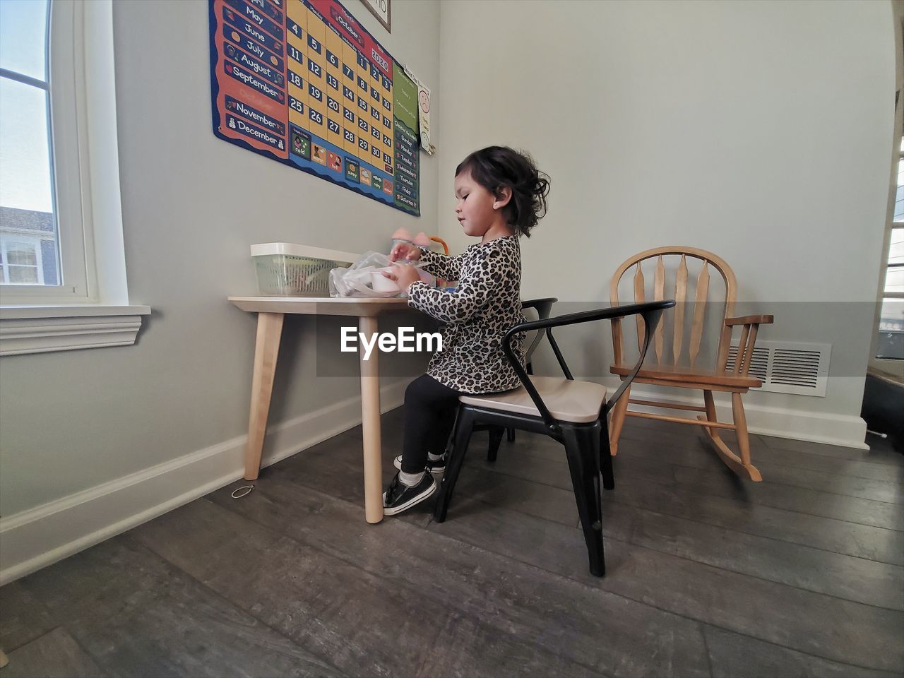 SIDE VIEW OF WOMAN SITTING ON TABLE AGAINST WINDOW