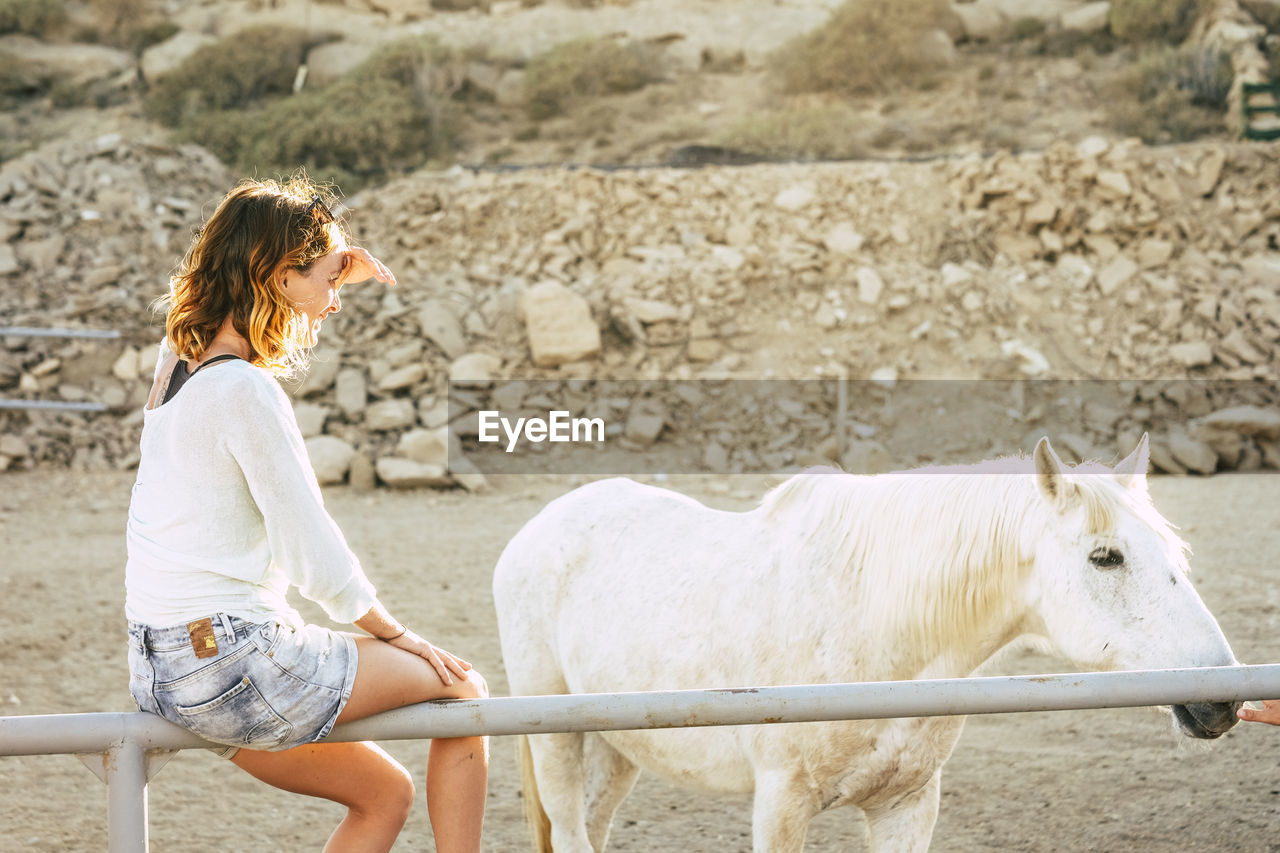 Woman sitting by pony on railing in ranch