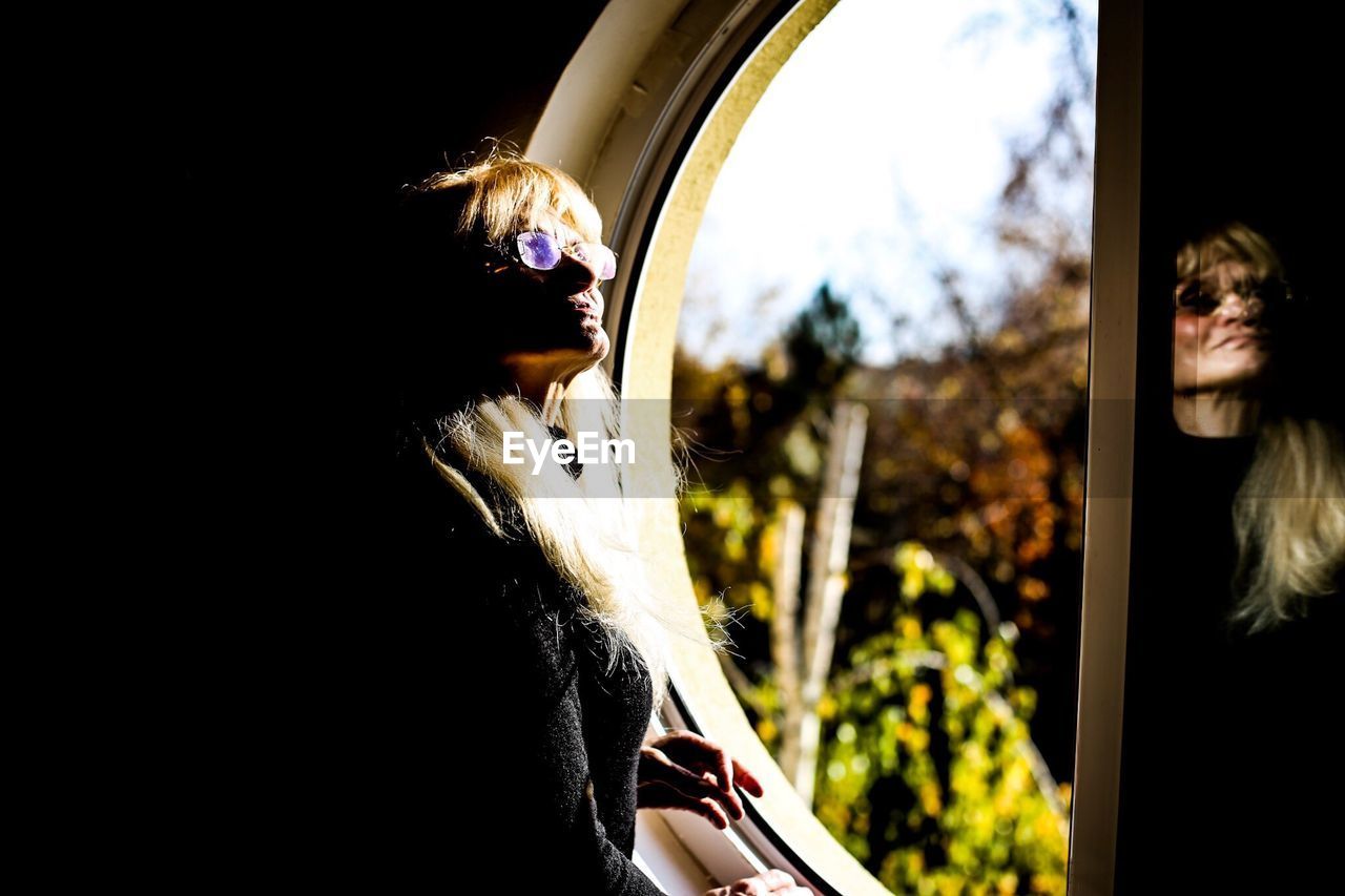 Senior woman wearing sunglasses while standing by window