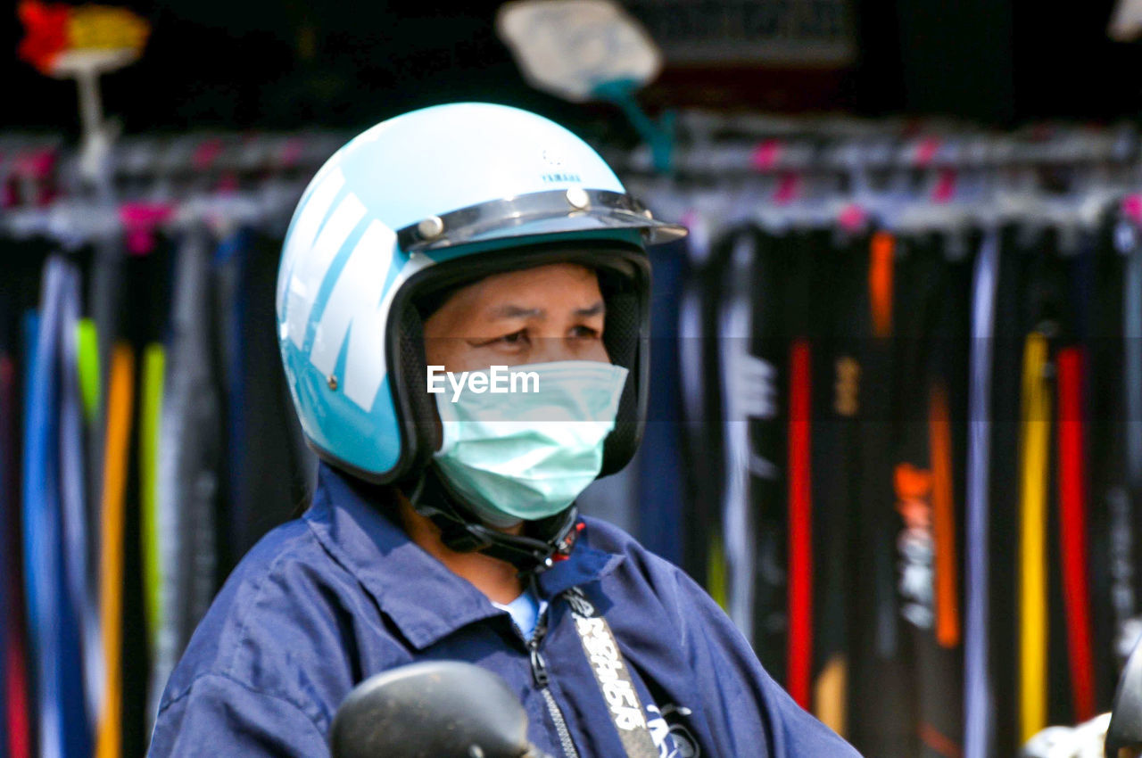 Woman wearing mask and helmet riding scooter at city