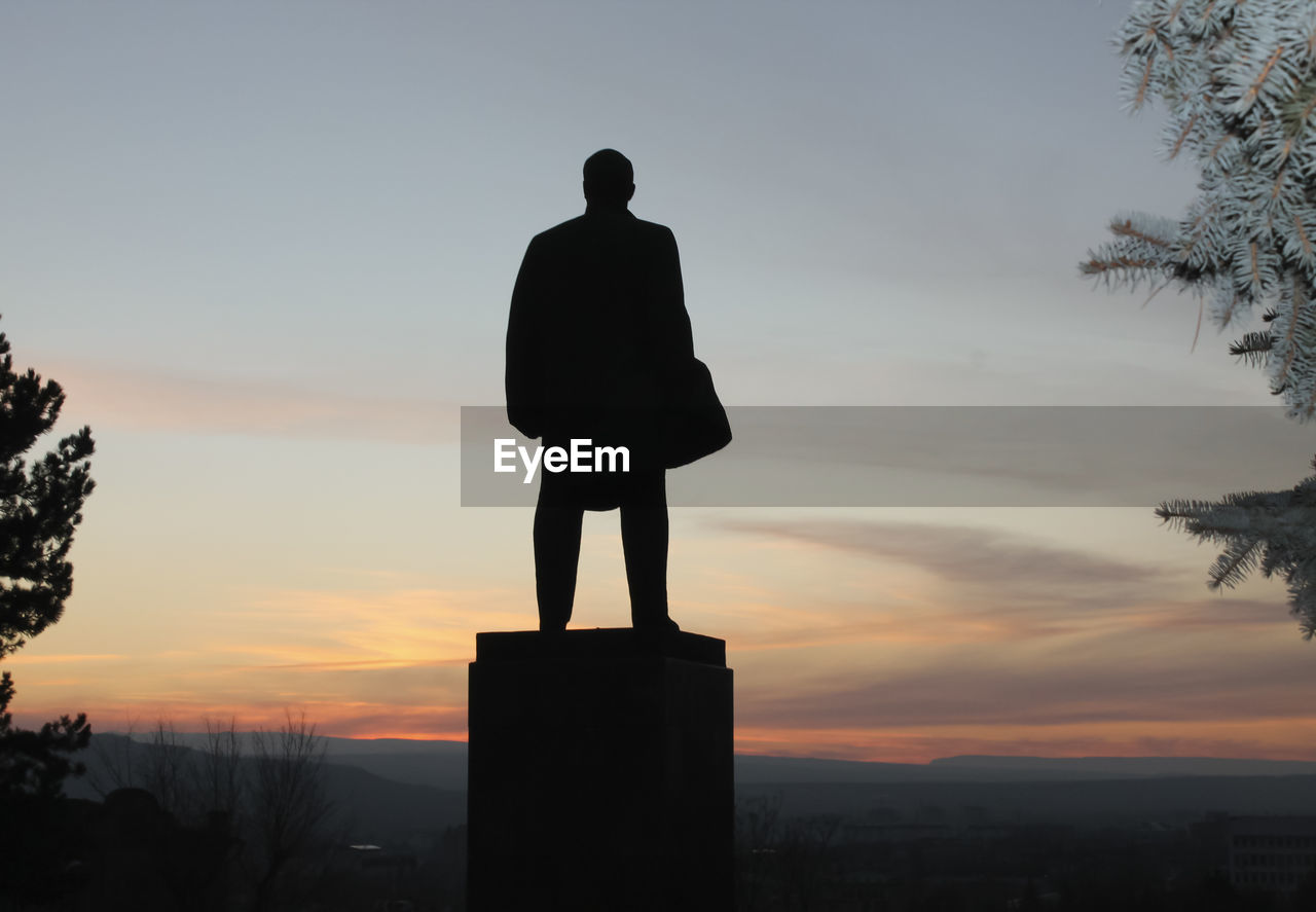 rear view of silhouette man standing on field against sky during sunset