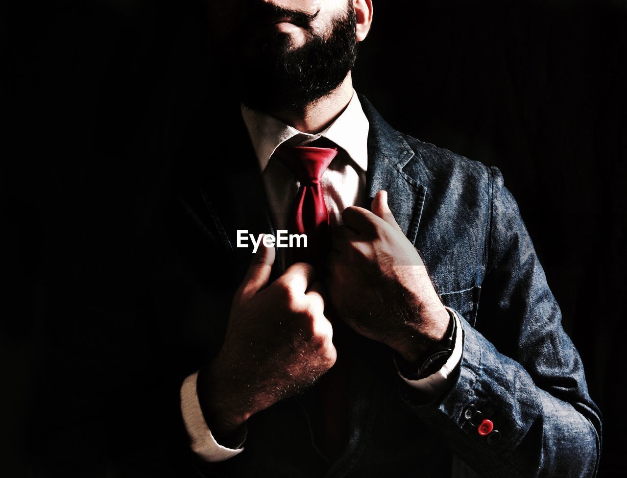 Midsection of businessman in suit and tie against black background