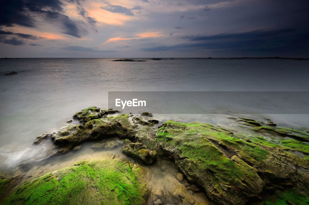 Rock formation at sea against sky during sunset