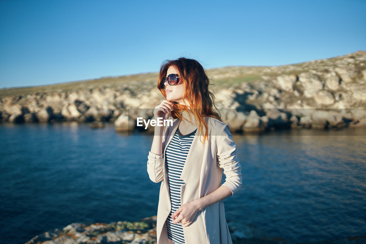 Woman wearing sunglasses standing by sea against sky