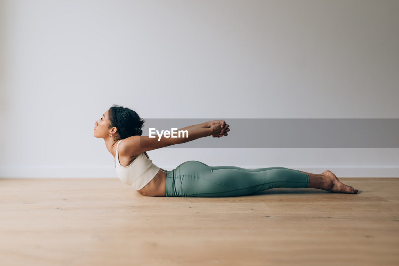 Yoga teacher practicing yoga position of cobra against white wall and wood floor with copy space