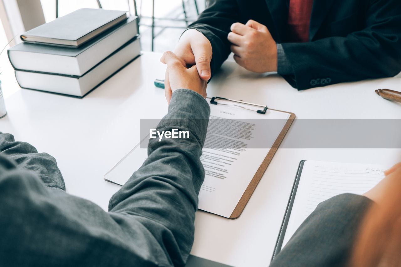 Midsection of lawyer shaking hands with colleague while sitting at desk