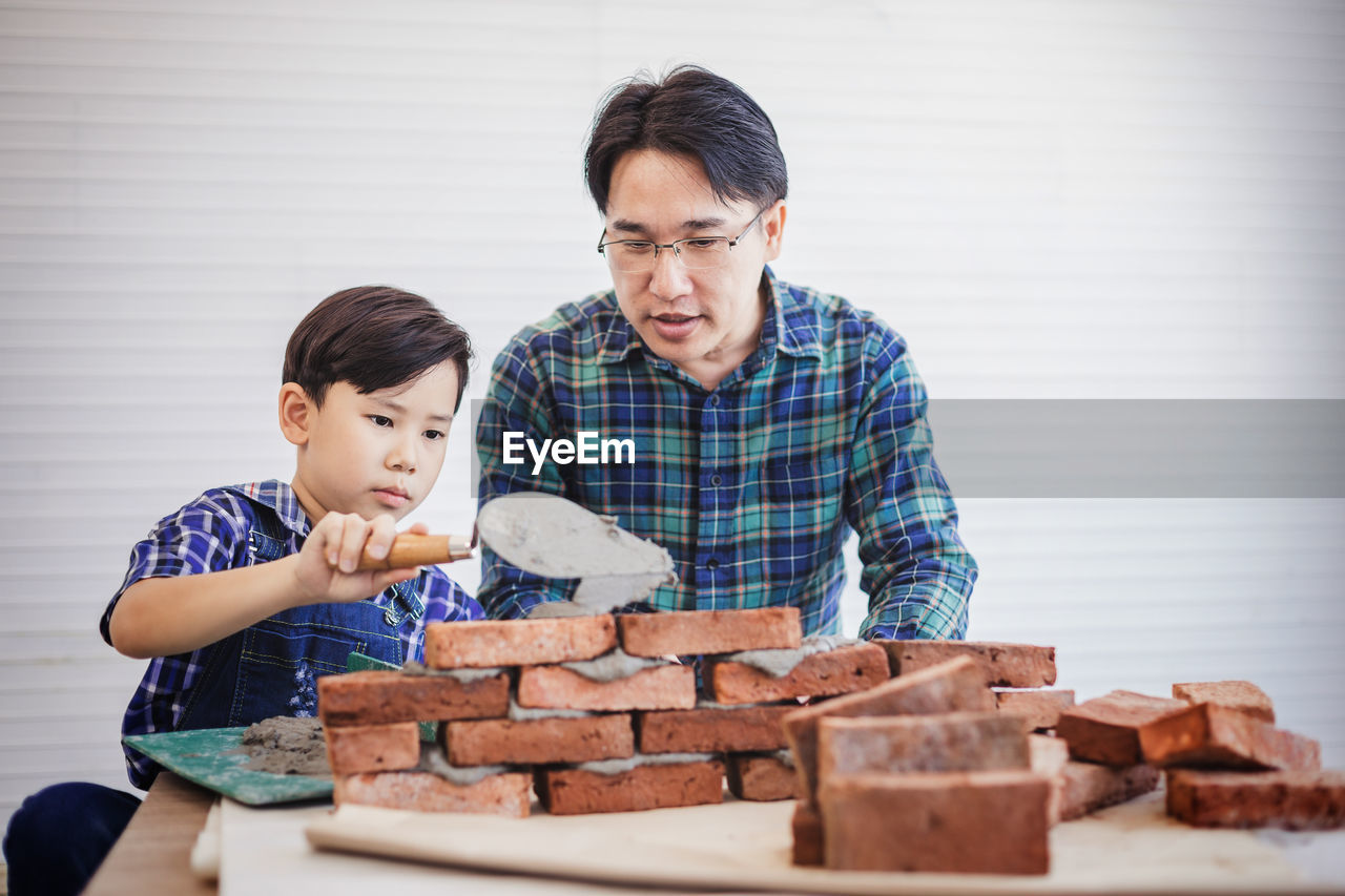 Father teaching son to make brick wall at workshop