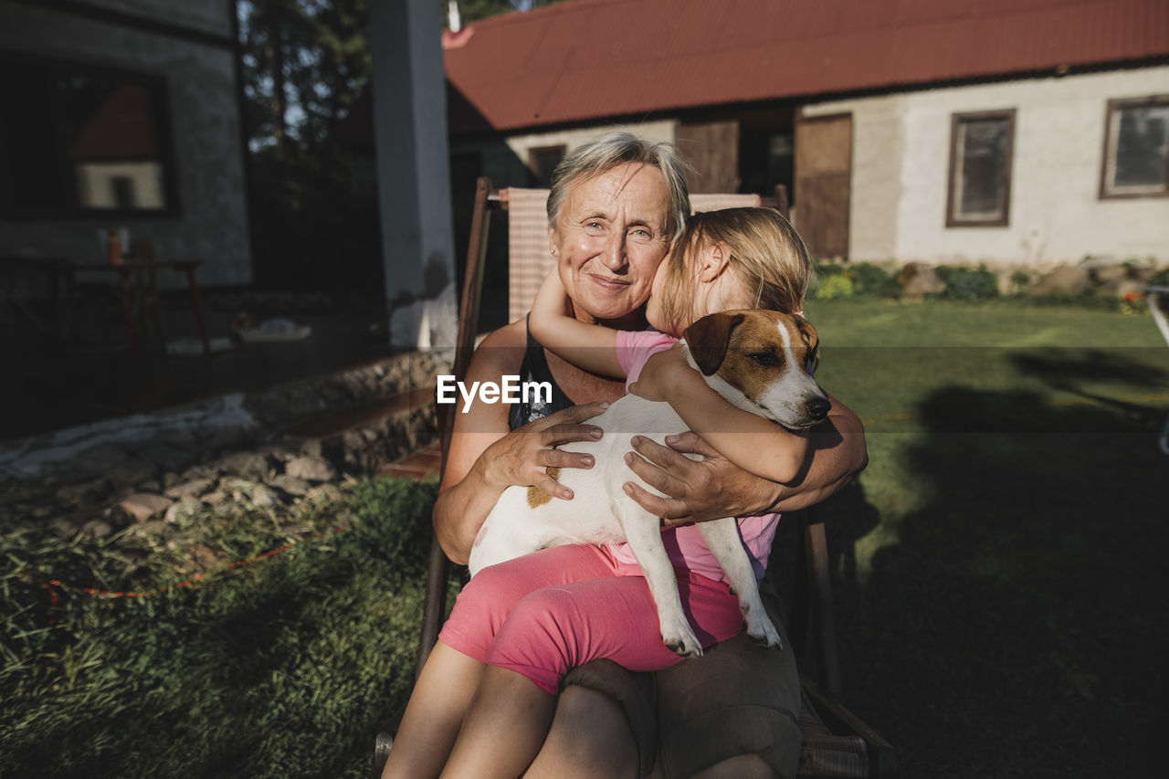 Smiling grandmother with granddaughter and dog on deckchair in garden