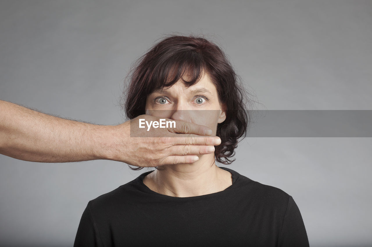 Cropped image of hand covering woman mouth against white background