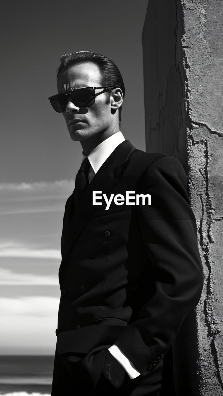 portrait of young man wearing sunglasses standing against wall