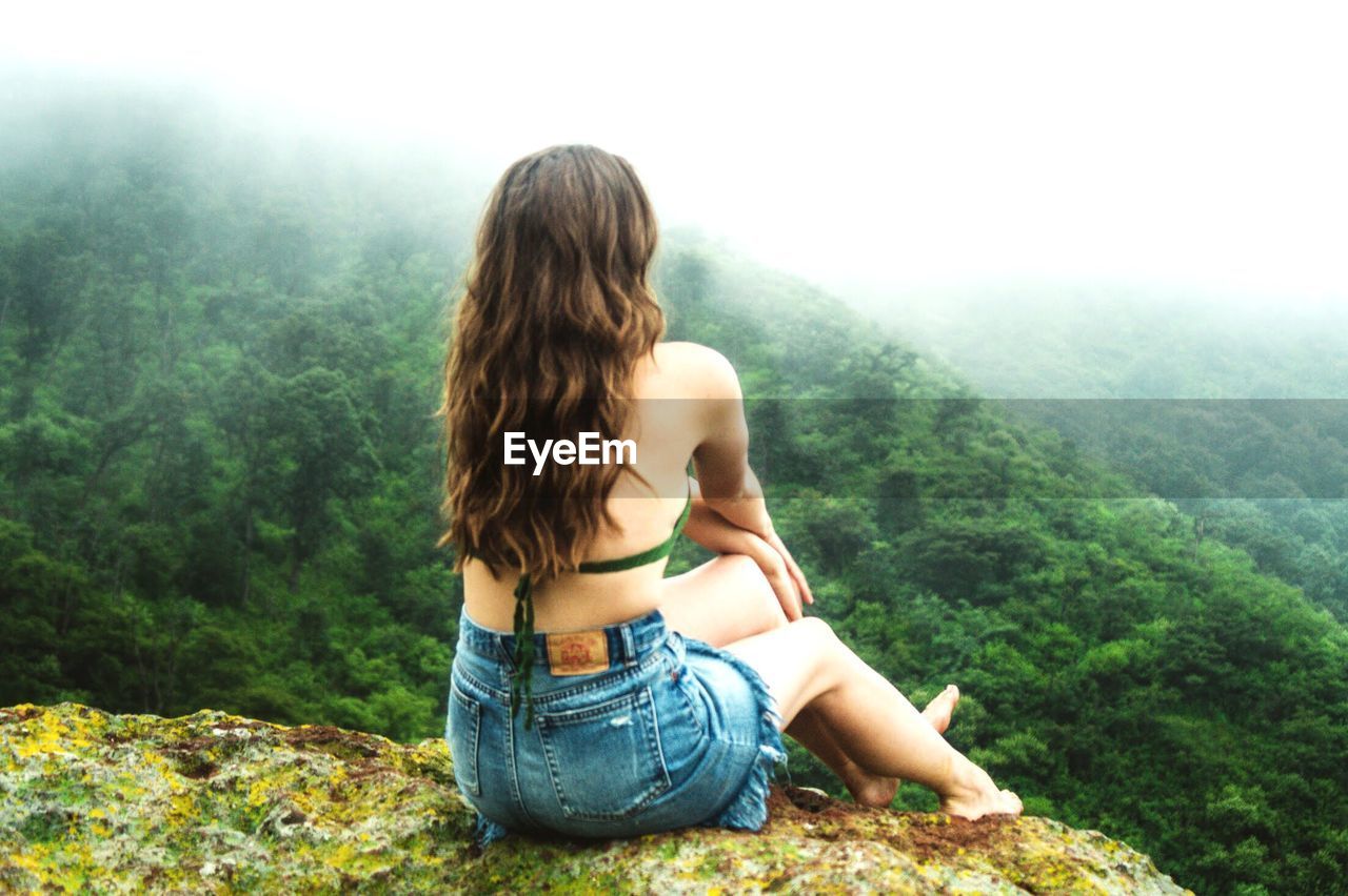 Rear view of young woman looking at mountains during foggy weather