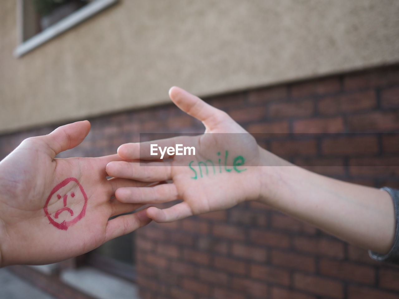 Cropped hands with anthropomorphic face and text on palms against building