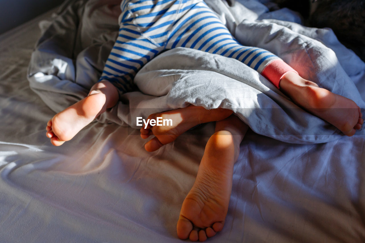 Elder child and smaller child feet in the parent's bed under blanket