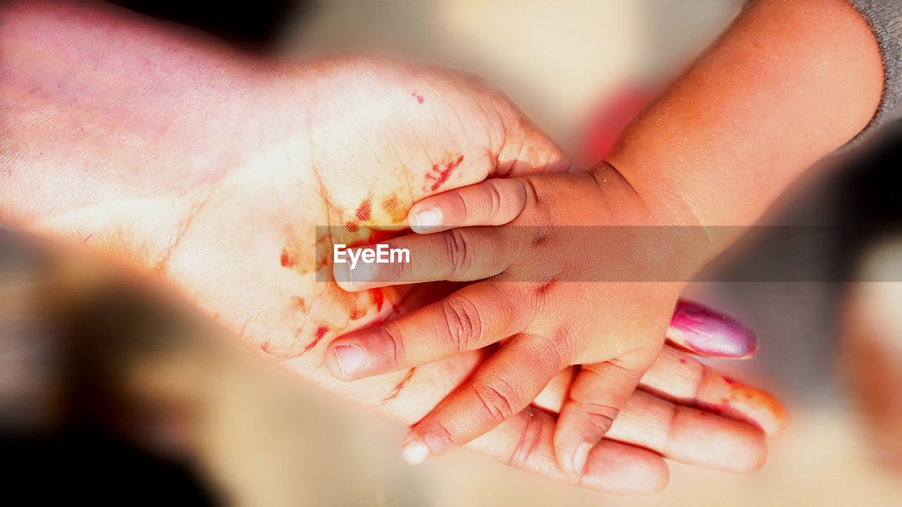 Cropped hand of mother and baby girl with blood at home