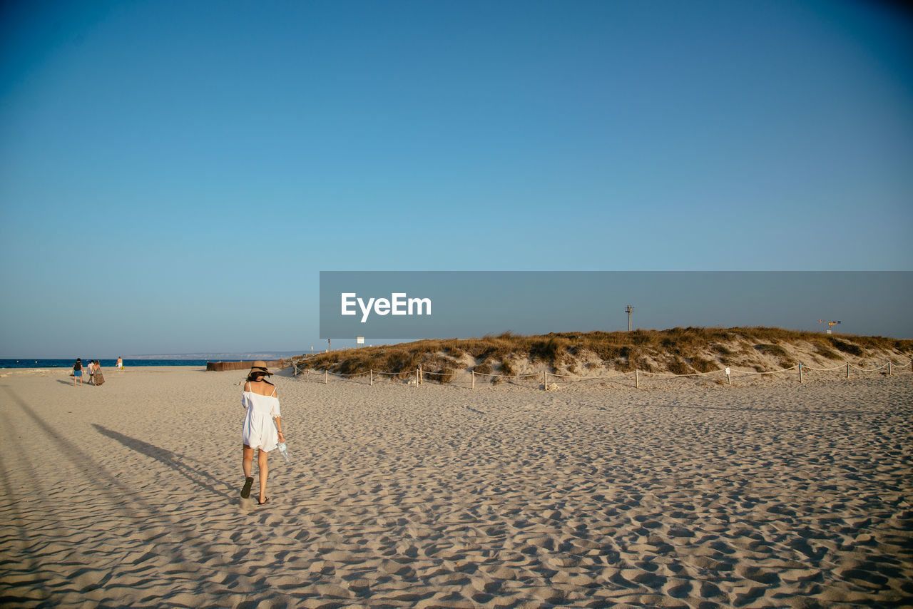 Rear view of woman walking on sandy beach