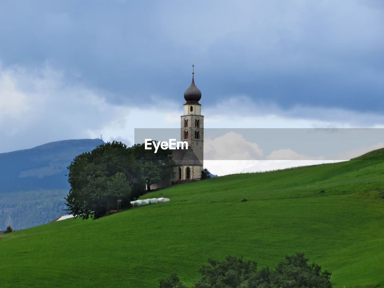 San valentino church by grassy field against cloudy sky