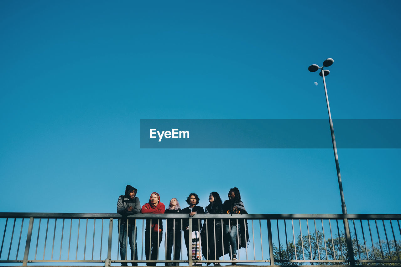 Low angle view of friends walking by railing on bridge