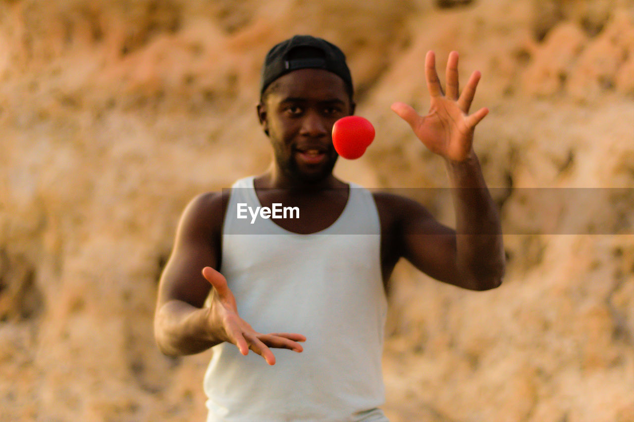Portrait of young man catching red heart shape against rock formation