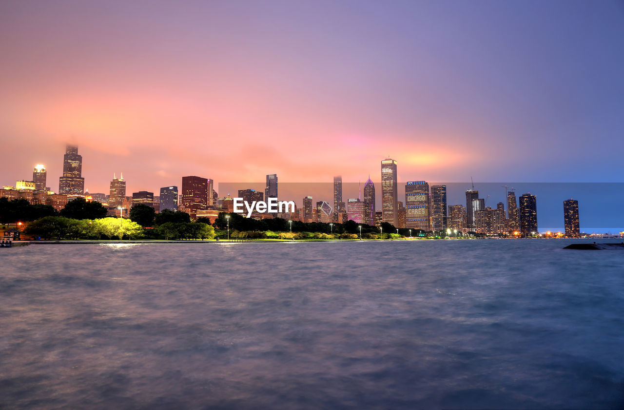 Sea by buildings against sky during sunset