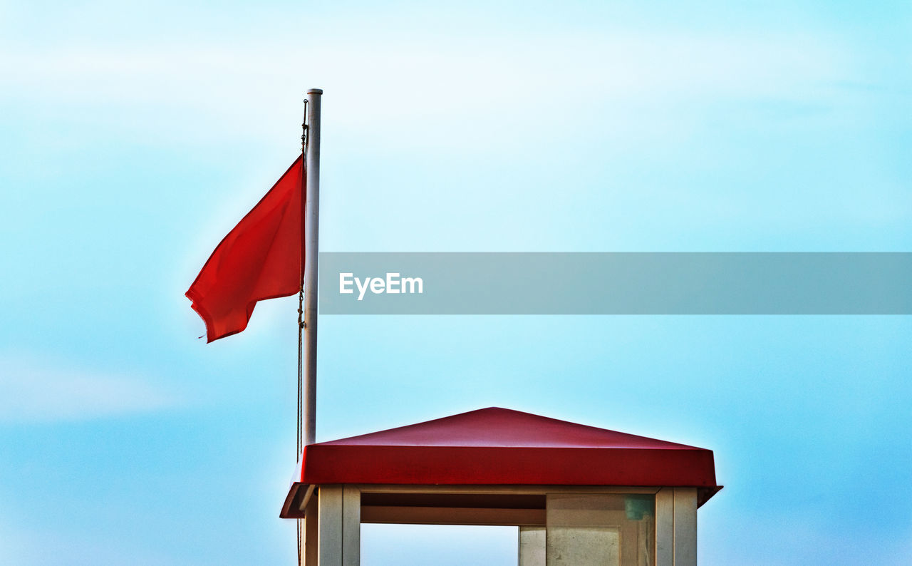 A bright warning flag near a lifeguard tower ,blue and cloudy sky