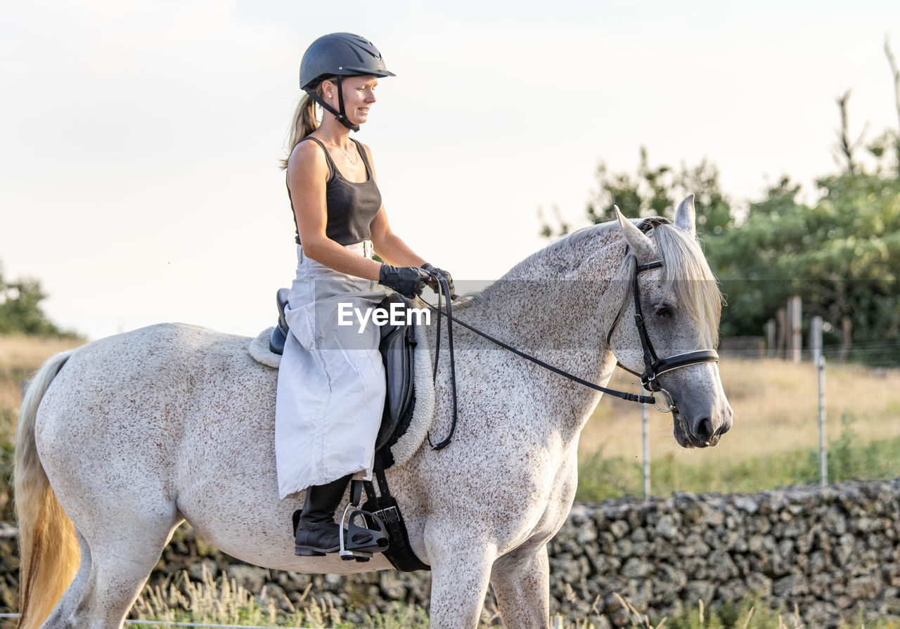 White lusitano mare, female dressage rider, outdoors on sand.