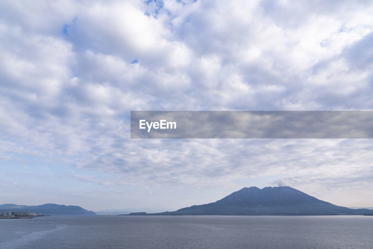 Scenic view of sea by mountain against sky