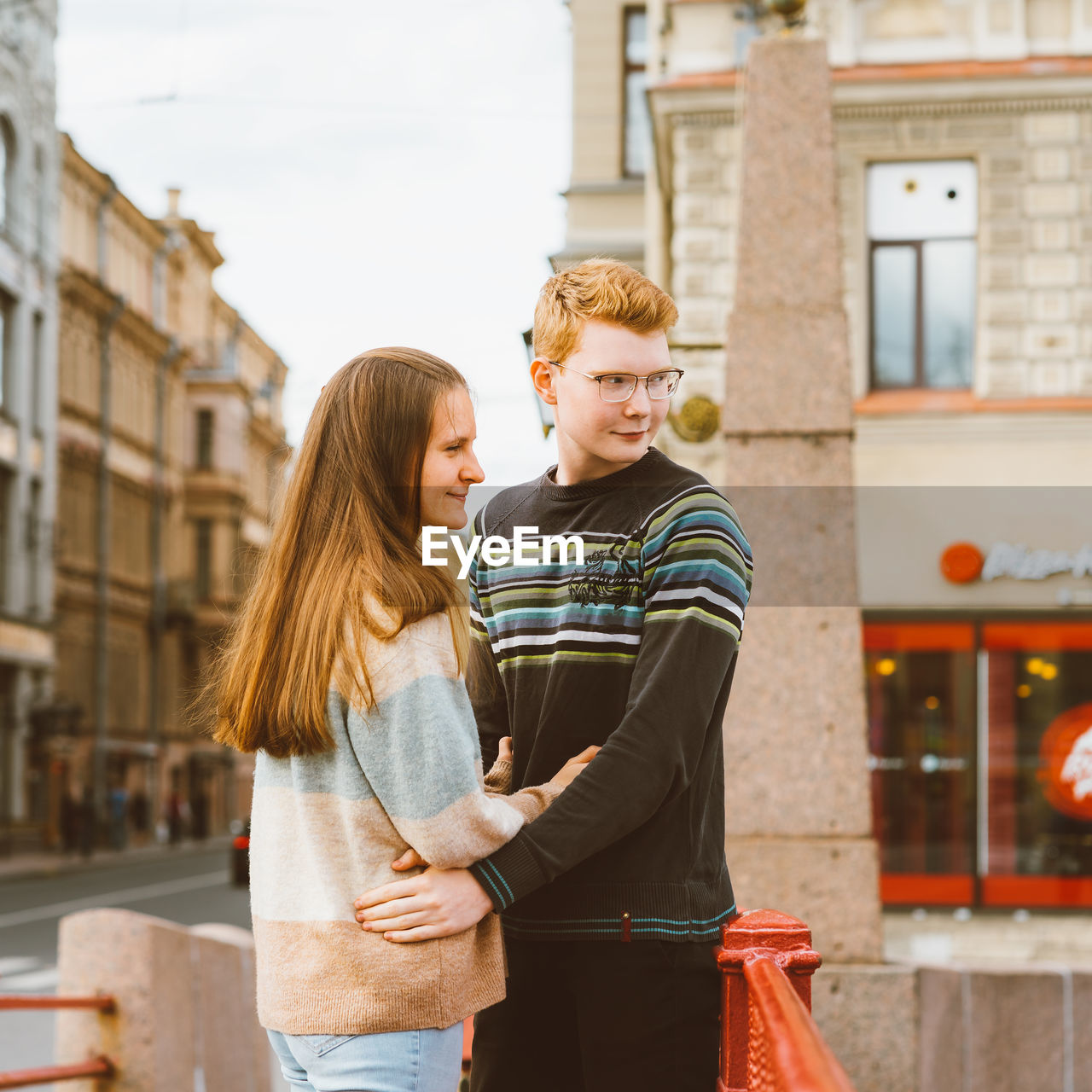 YOUNG COUPLE STANDING ON CITY STREET IN BACKGROUND