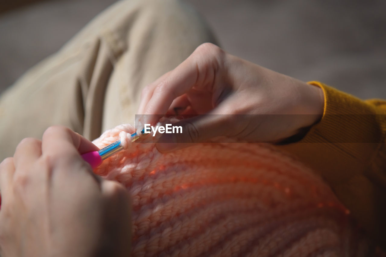 Female hands close-up, crocheting clothes on the sofa at home, handmade