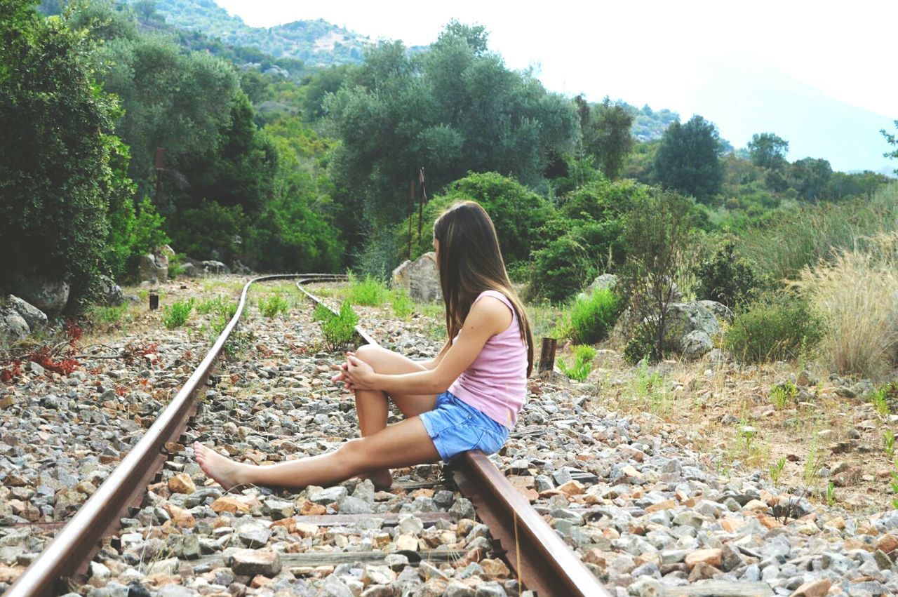 Side view of young woman sitting at railroad track