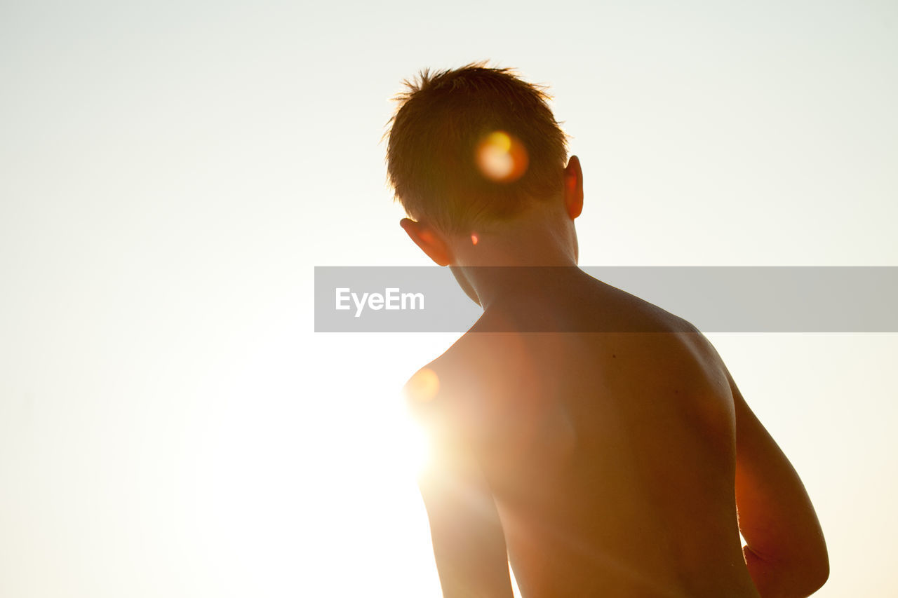 Silhouette shirtless boy against bright sky