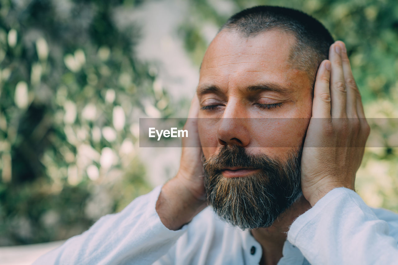 Man sitting with his eyes closed and doing a reiki auto treatment, holding hands on ears.