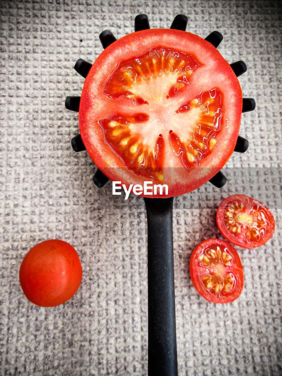 Half tomato on a toothed kitchen spoon on a gray ground. vertical image.