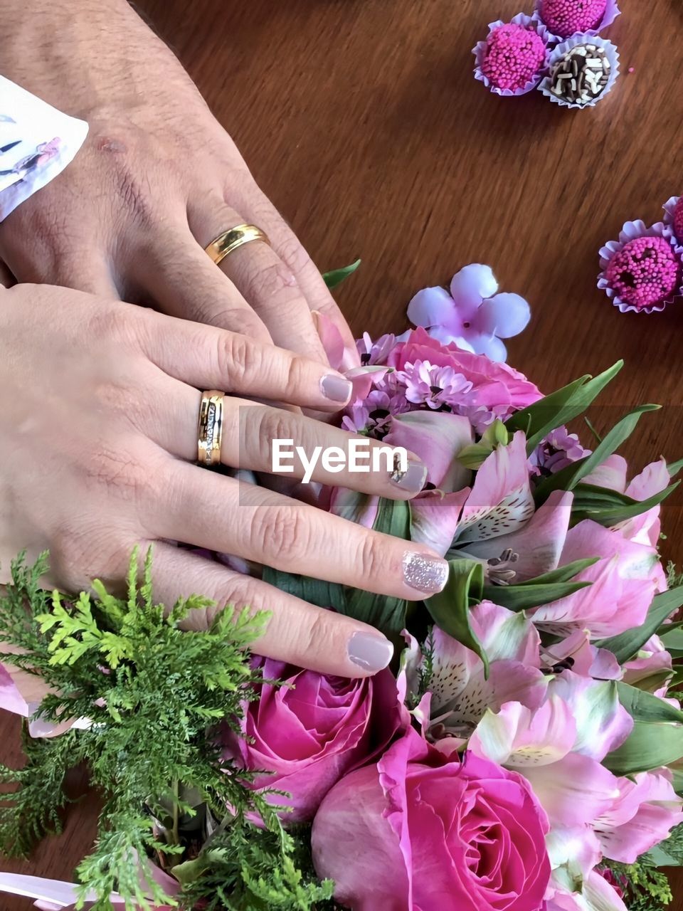 CLOSE-UP OF PINK FLOWERS ON HAND AGAINST PURPLE FLOWERING PLANTS