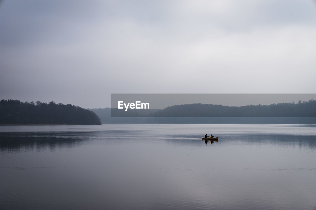 PEOPLE ON BOAT IN LAKE AGAINST SKY