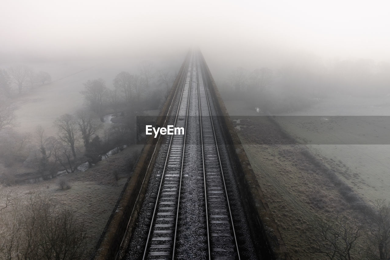 Aerial landscape above railway tracks on an old viaduct disappearing into the fog in the distance