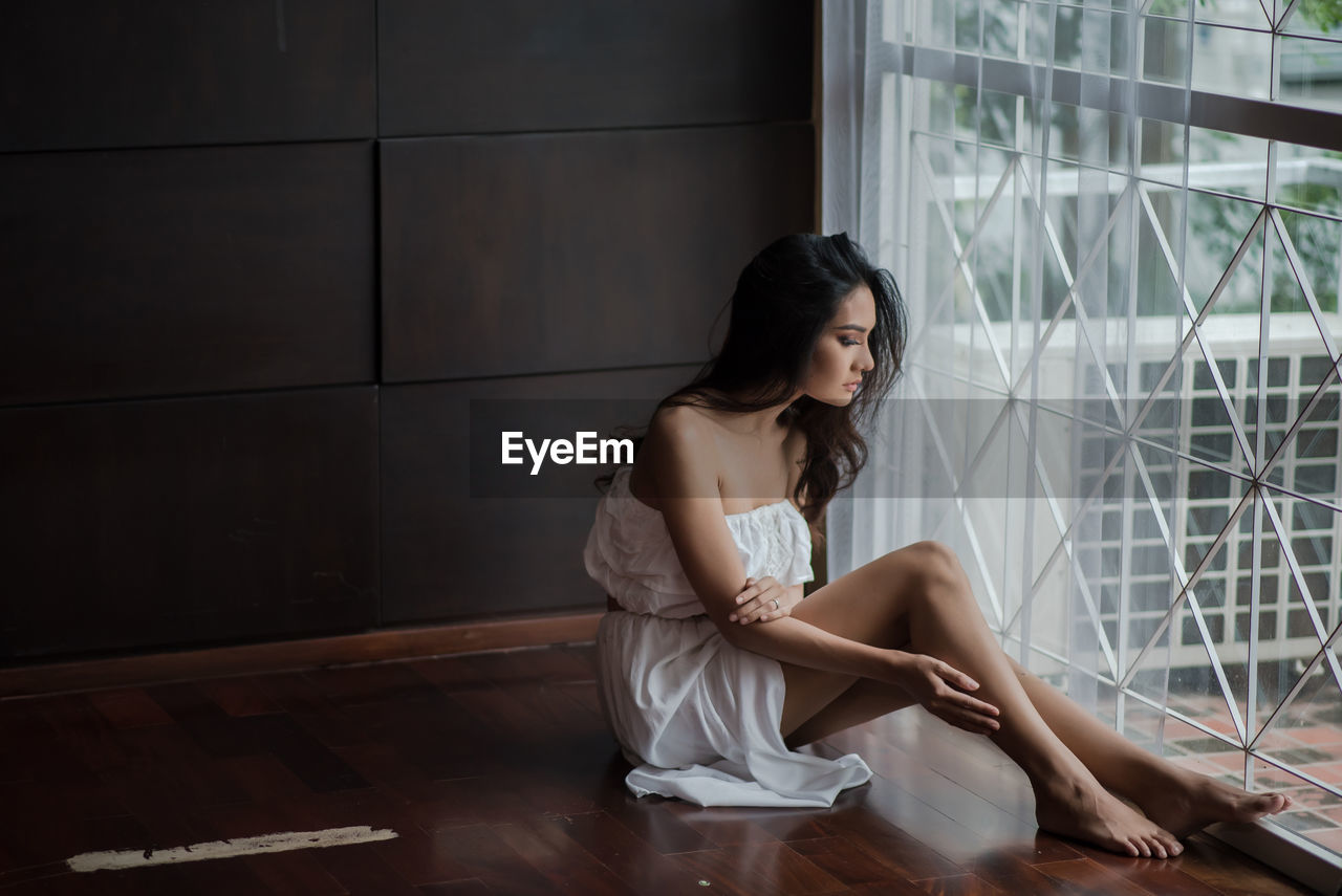 Full length of young woman sitting by window at home