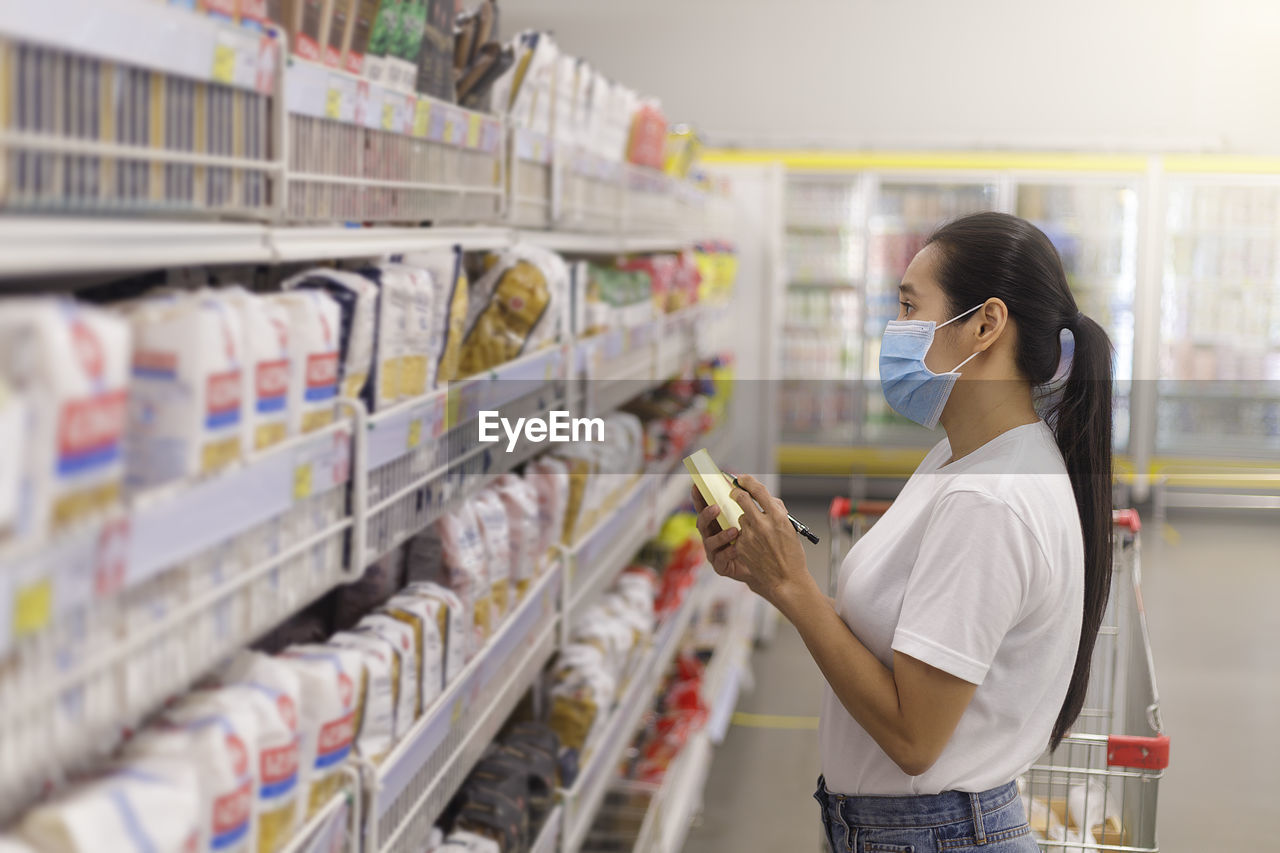 side view of woman holding shopping bags while standing in supermarket