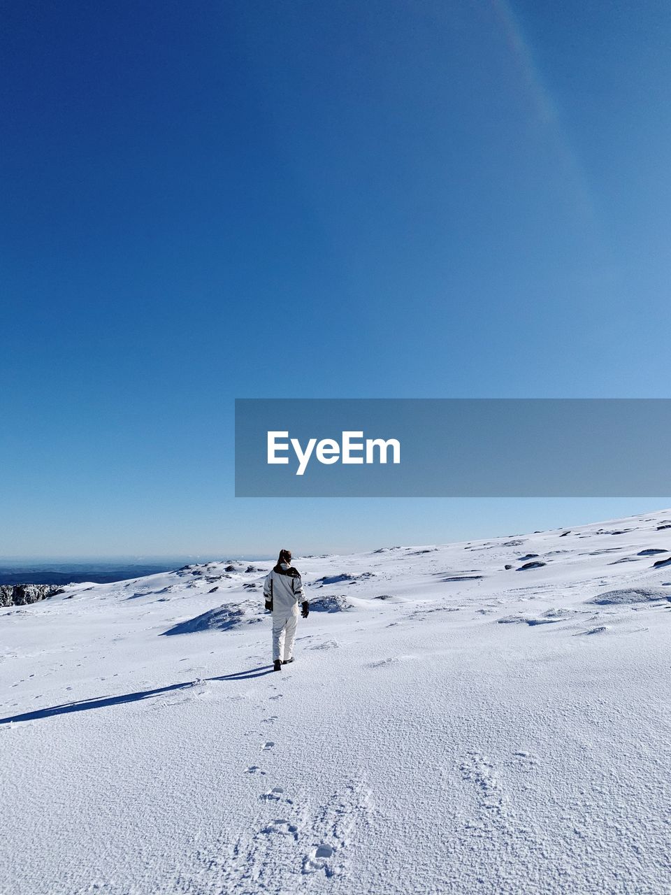 Woman on snowcapped mountain against clear blue sky