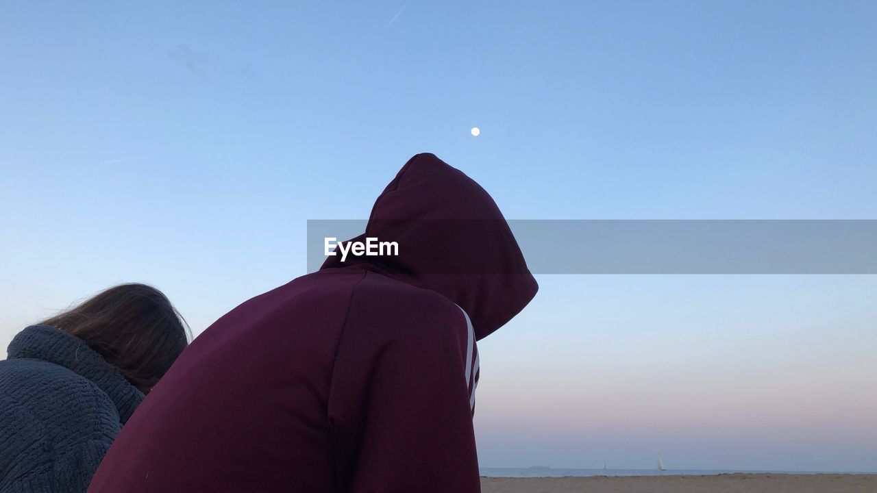 Side view of man and woman relaxing at beach against clear sky