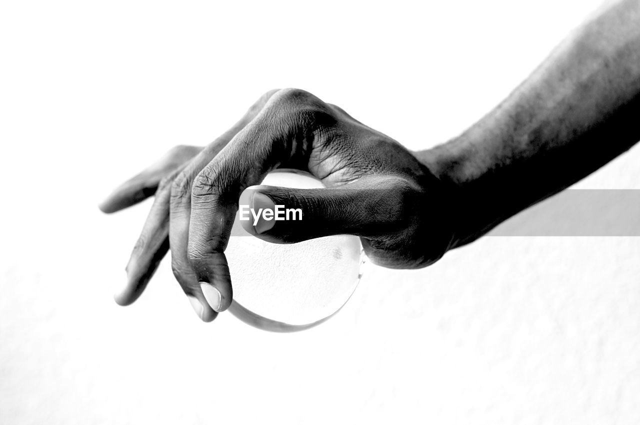 Close-up of hand holding ball against white background