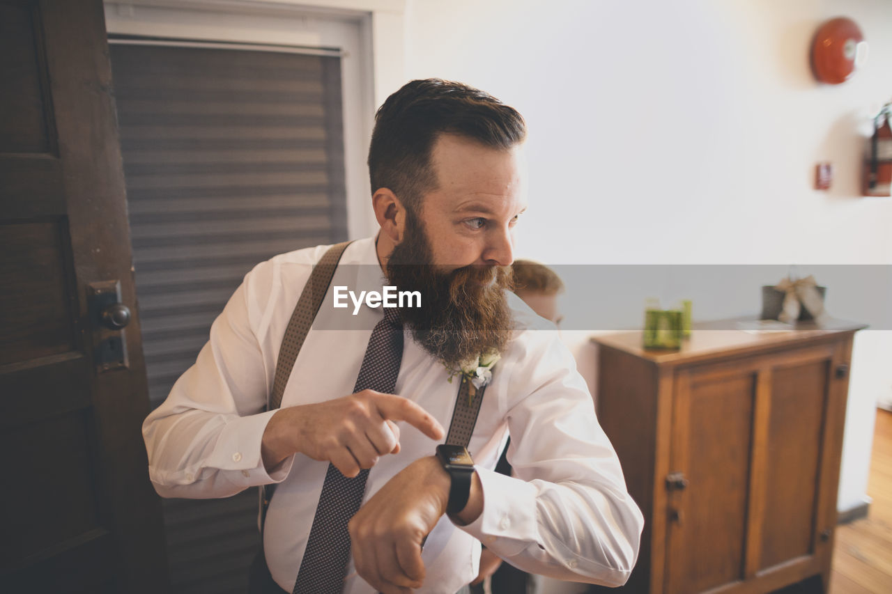 Bridegroom pointing towards wristwatch while pageboy standing behind at home