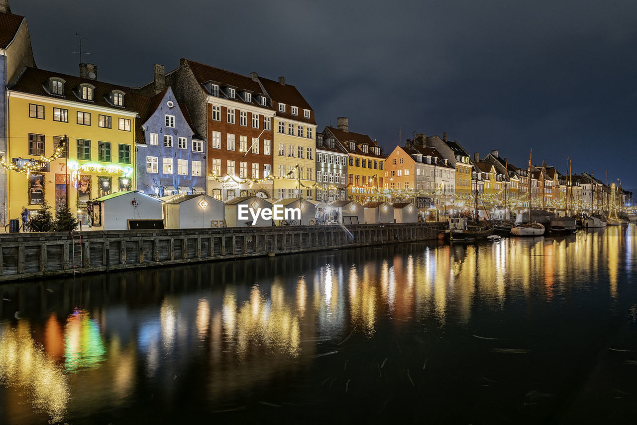 Reflection of illuminated buildings by river against sky at night