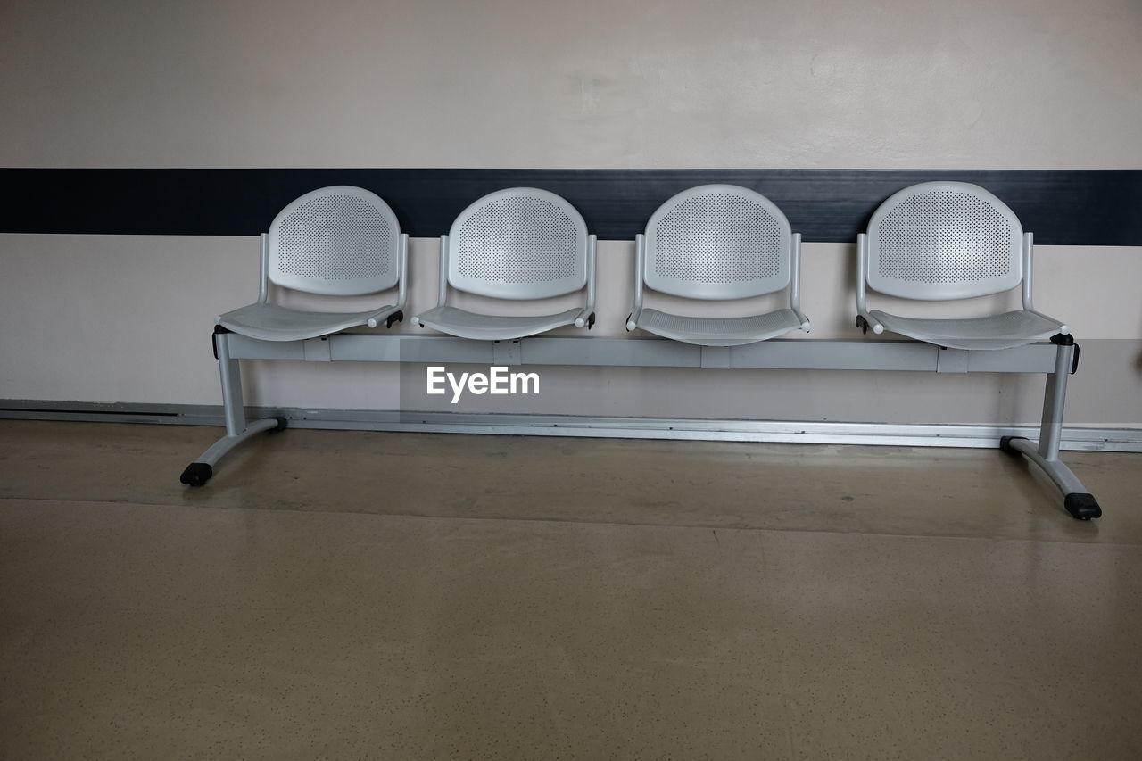 EMPTY CHAIRS AND TABLE AGAINST WHITE WALL IN ROOM